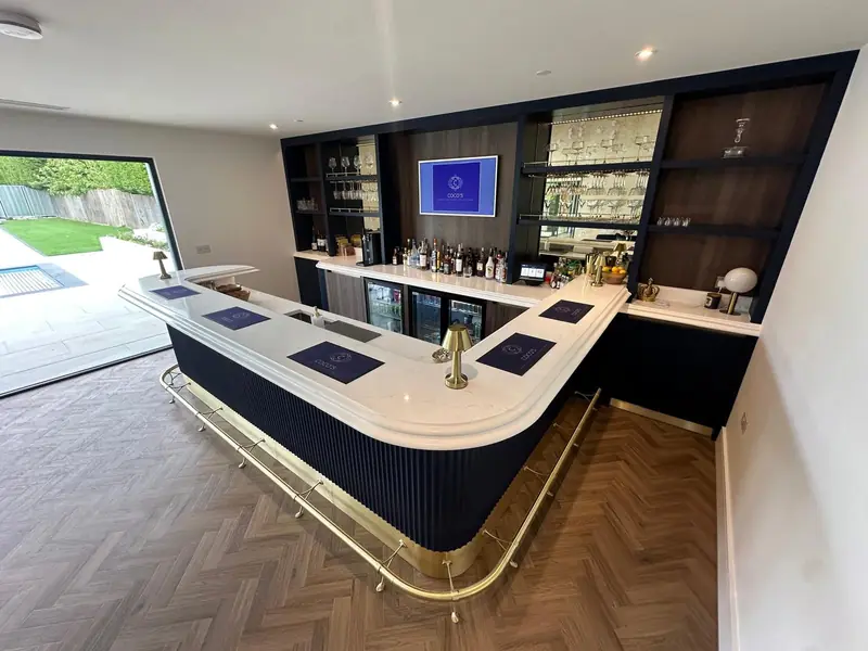 Curved bar with a fluted navy front, white worktop and brass foot rail